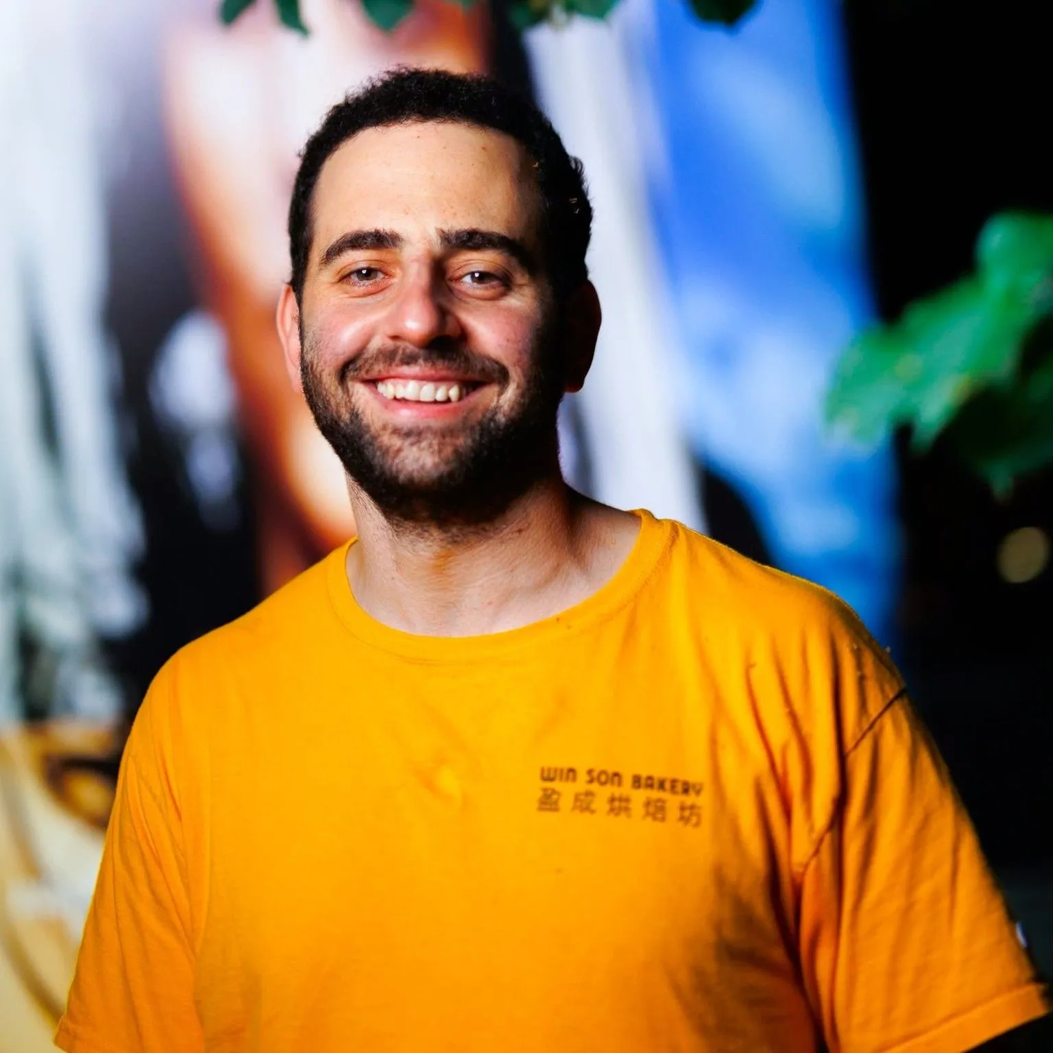 DANIEL GENEEN smiling in a bright yellow shirt against a colorful backdrop