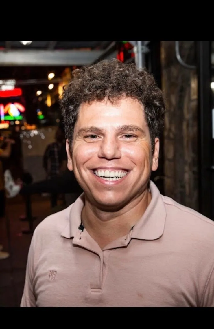 DOMINIC LEONELLI smiling in a tan polo on a patio at night