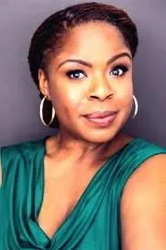 MUGGA in an emerald green draped top with gold hoop earrings
