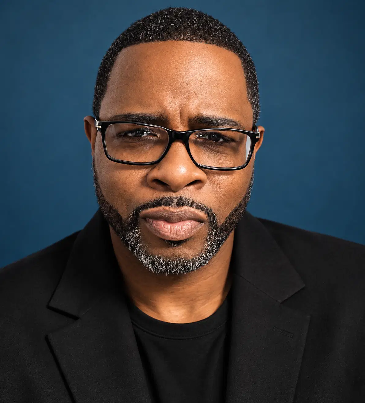 Shawn Cornelius in a black blazer and glasses against a blue studio background