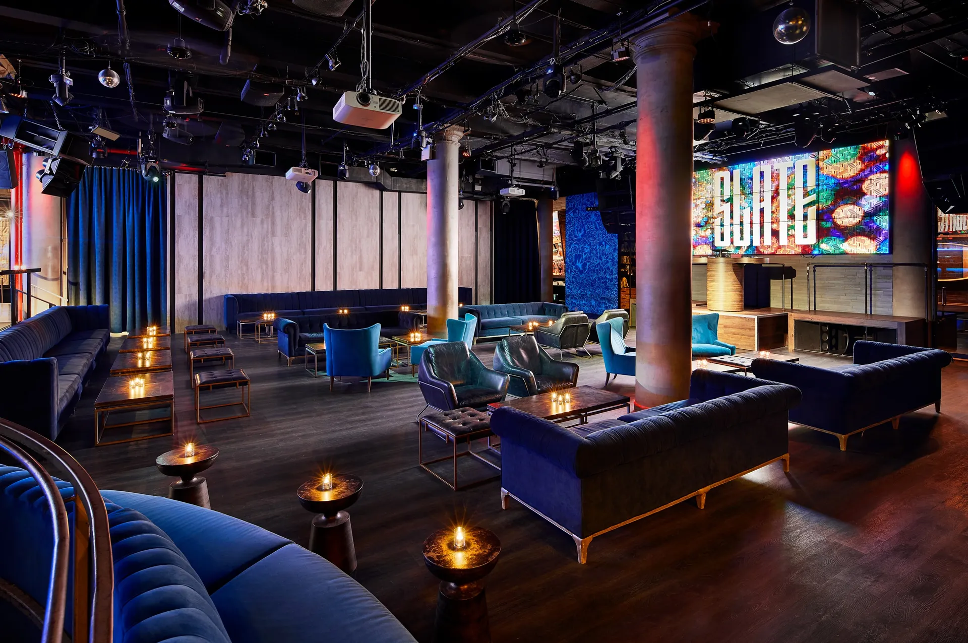 Slate NYC lounge with blue seating and a stage screen